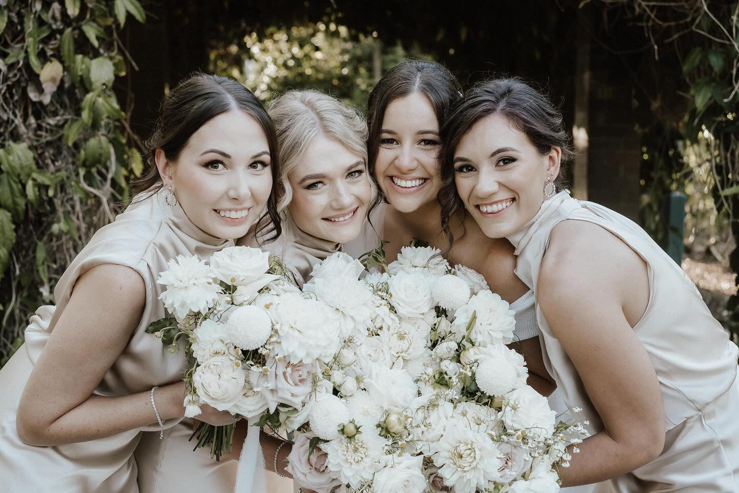 Four women posing together with white bouquets in a natural setting in Brisbane for a wedding.