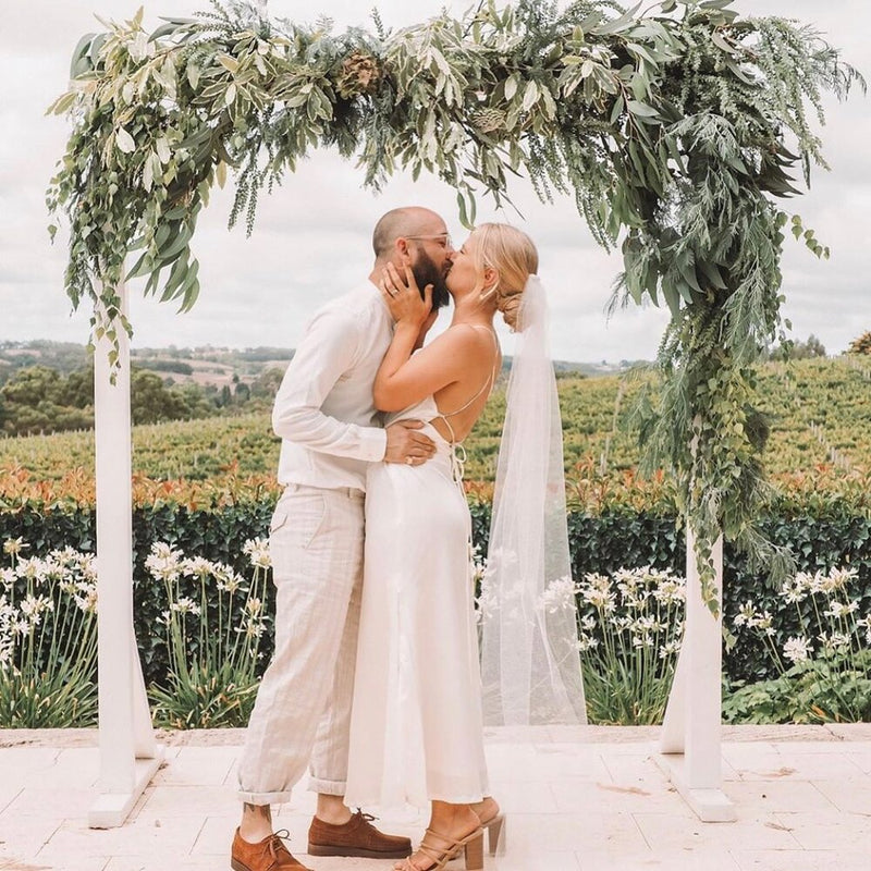 Couple kissing under a floral archway with a scenic background in the Adelaide Hills.