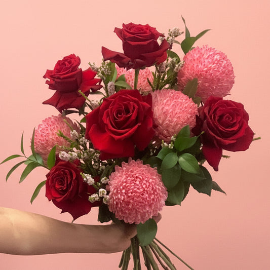 Bouquet of red roses and pink flowers held against a pink background