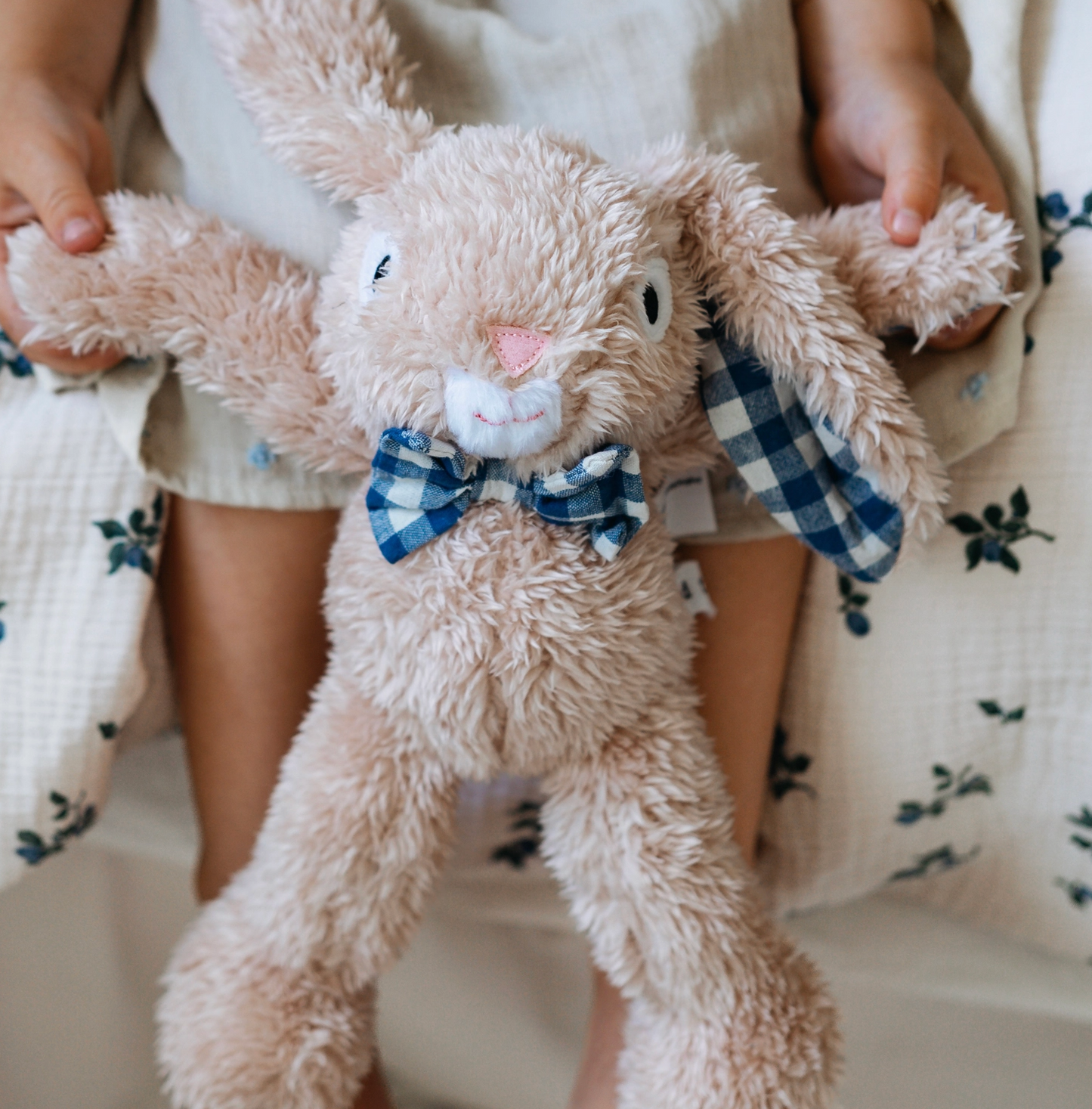 Stuffed bunny toy with a bow tie held by a child in a floral dress.