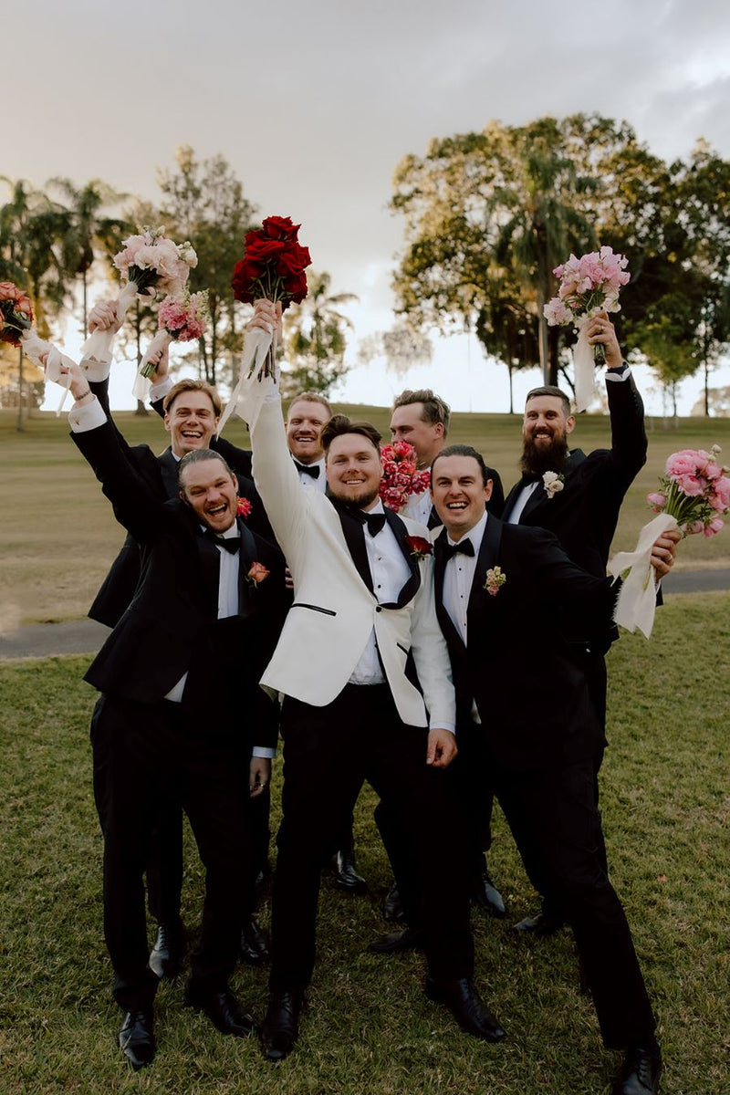 Group of men in suits holding bouquets outdoors on a grassy area