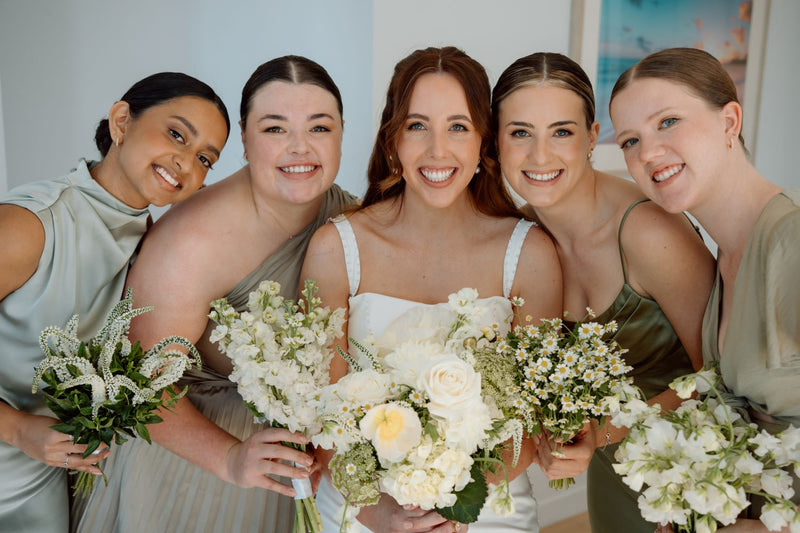 Bride with bridesmaids holding floral bouquets of single flower varieties and poppies in white and green,  indoors