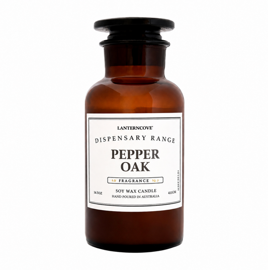 A 16oz amber glass apothecary-style candle bottle with a black screw cap and a white label reading 'Lanterncove Dispensary Range Pepper Oak Fragrance'.